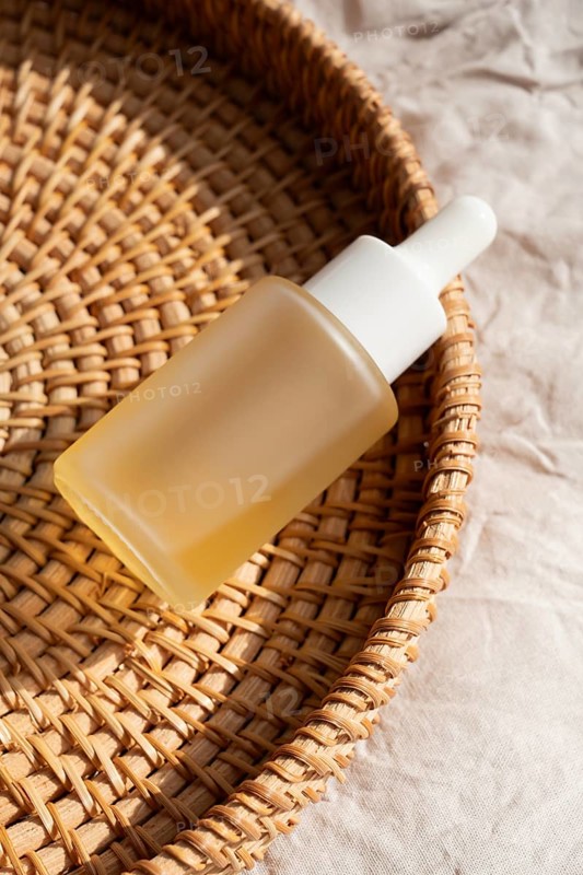 A minimalist glass dropper bottle rests on a woven basket under gentle sunlight. The scene exudes tranquility and natural beauty, perfect for promoting skincare cosmetics
