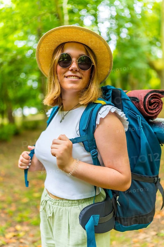 Vertical portrait of a young woman wearing a backpack smiling while walking through a forest path