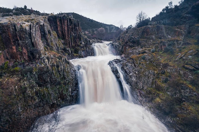 Majestic view of the cascading waters at Cascada del Aljibe, set amidst rugged cliffs and lush vegetation in Guadalajara, Spain, presenting a serene yet powerful natural scene