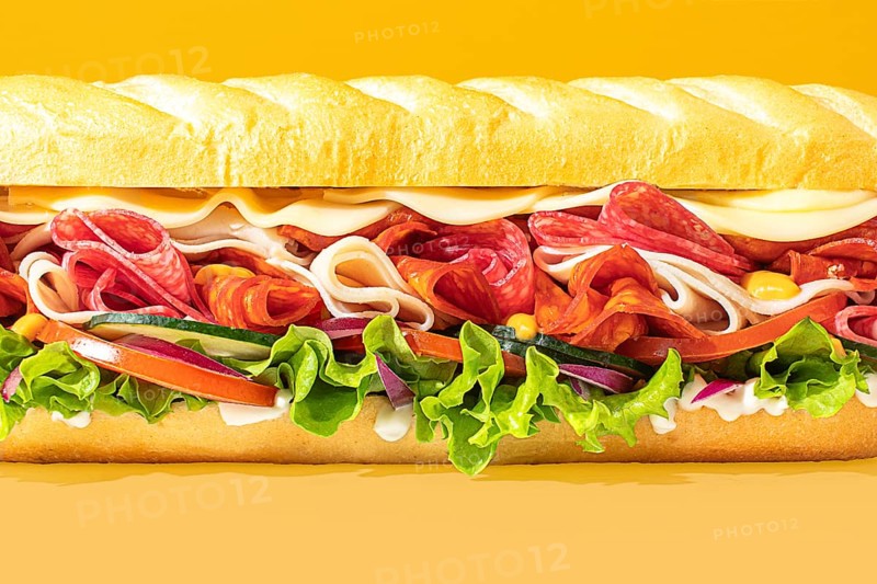 Close-up of a stacked deli sandwich, styled on a vibrant monochrome backdrop, with frontal lighting to emphasize depth and detail