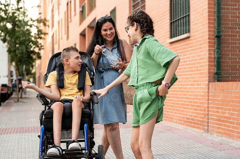 A family shares a joyful moment outdoors with a girl with a tracheostomy and a boy with cerebral palsy. The bond and happiness are evident as they enjoy the day