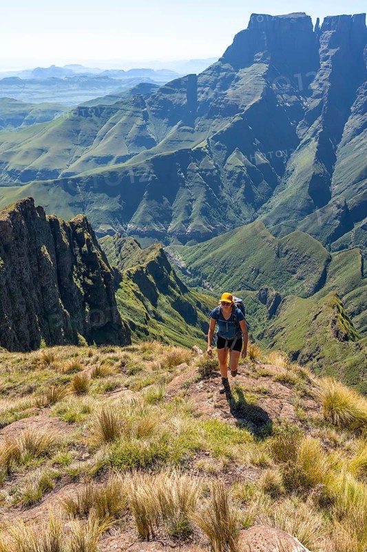 Young hiker looking at the impressive mountains and cliffs of the Drakensberg Mountains, hiking trail on the Sentinel Hiking Trail, Drakensberg, KwaZulu-Natal, South Africa