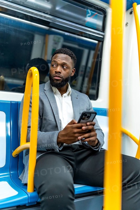 Young businessman riding a subway train, using a smartphone while glancing away, immersed in communication and digital connection