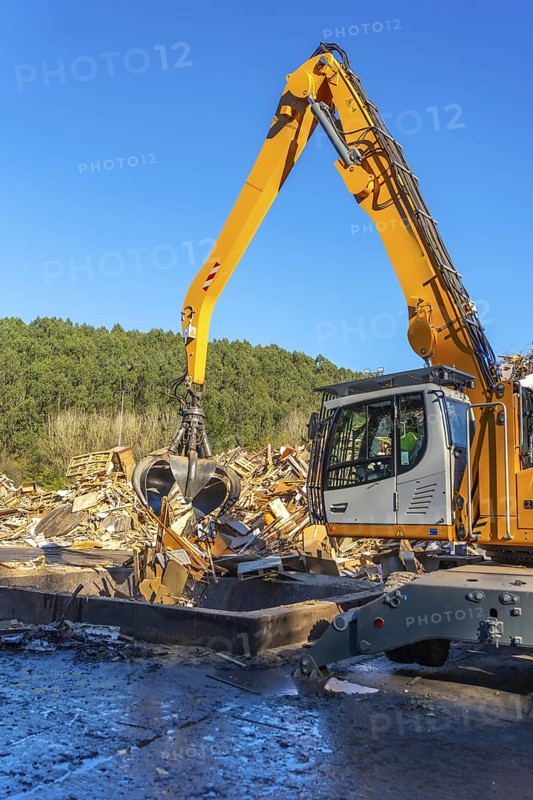 Vertical photo of an excavator moving waste outside a recycling plant