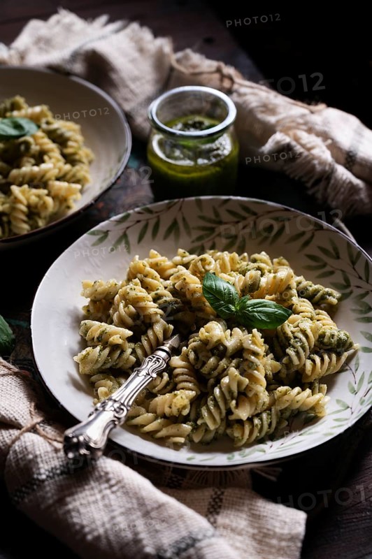 A rustic bowl of spiral pasta tossed in vibrant green pesto sauce, adorned with fresh basil. An inviting dinner scene with soft, warm lighting and loaf of bread