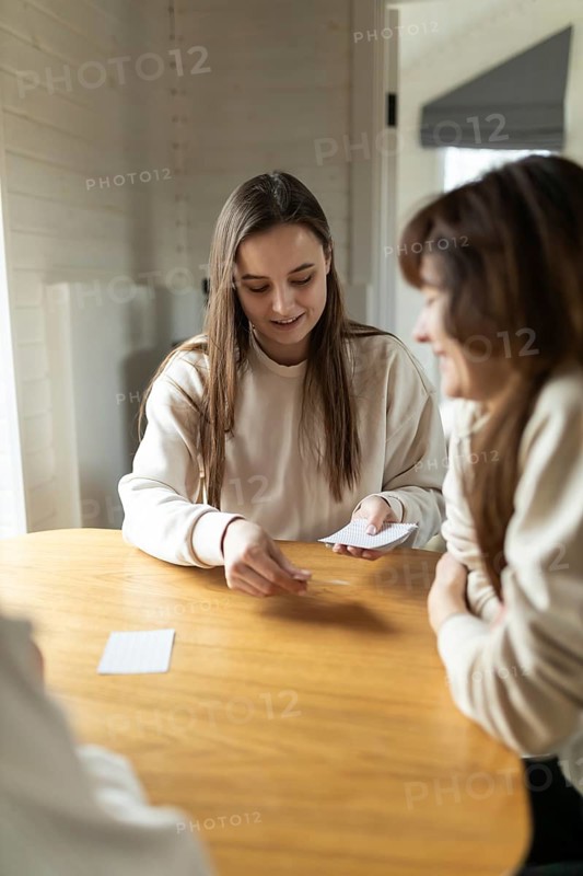 A joyful group of friends gathers around a warm, wooden table, engaging in a fun card game. The atmosphere is relaxed, highlighting friendship and leisure time indoors