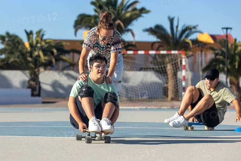 A teenager with Down syndrome enjoys sports with his family, promoting inclusion and joy They participate with an outdoor skateboard, highlighting support and unity