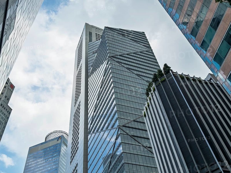 From below a captivating view of modern skyscrapers in Singapore, showcasing reflective glass facades against a cloudy sky, with greenery accents on the buildings