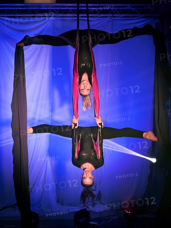 Two trapeze artists acrobats in vibrant costumes perform a breathtaking duo silk routine. The performers gracefully hang upside down, displaying strength and balance