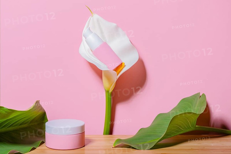A delicate pink cosmetic jar placed beside a vibrant calla lily flower against a soft pink background, ideal for beauty and skincare promotions