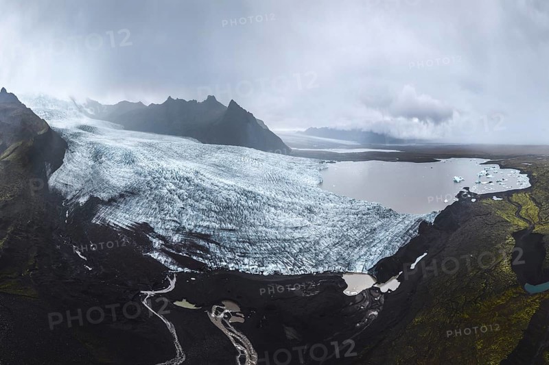 Aerial view of the vast Vatnajökull Glacier within Vatnajökull National Park, displaying a dramatic expanse of ice against a backdrop of rugged mountains and cloudy skies, highlighting the natural beauty of Iceland's largest glacier