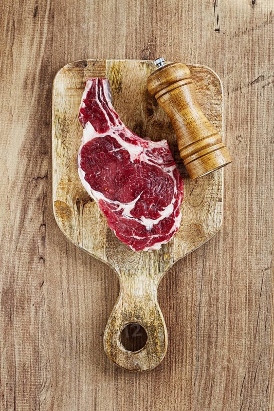 Raw rib eye steak, cowboy steak, on a wooden chopping board, top view, no people