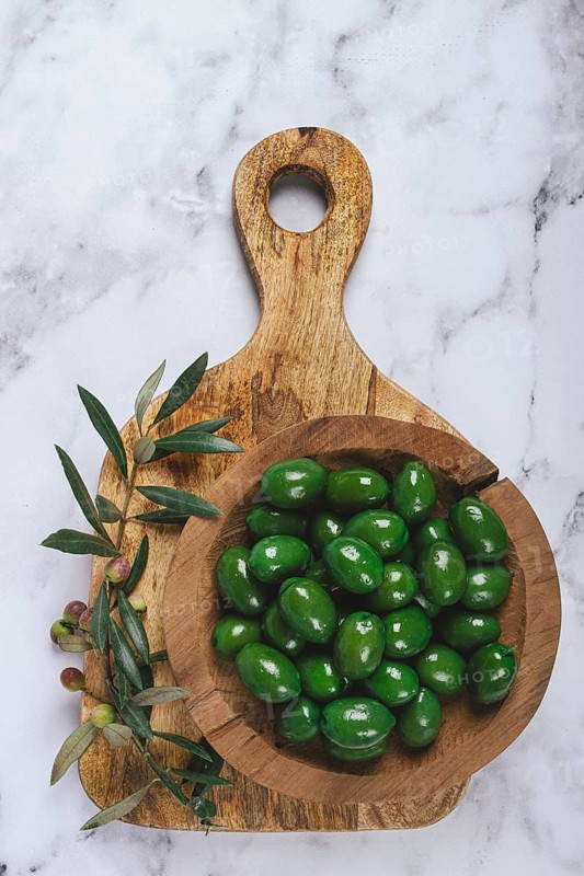 Halkidiki olives, classic Greek green olives, in a wooden bowl, on a cutting board, top view, without people