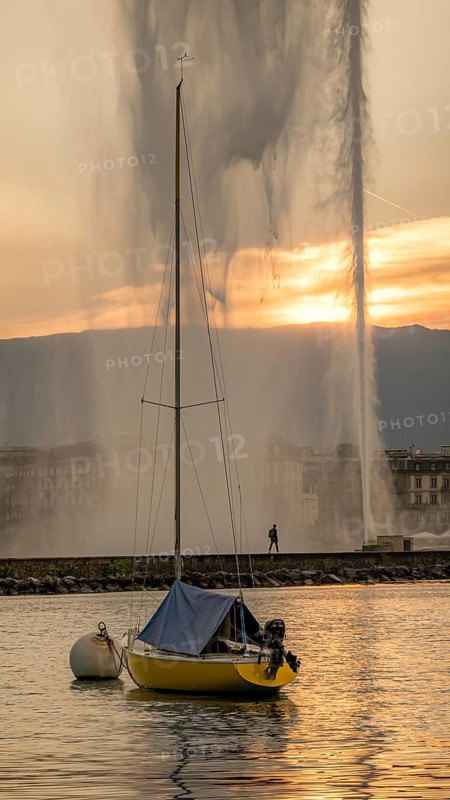 A serene scene captures a sailboat on Lake Geneva during a beautiful sunset, with the iconic Jet d'Eau fountain soaring in the background