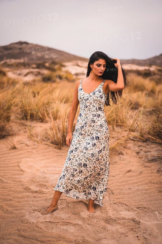 Portrait of a Caucasian brunette stroking her hair in a white floral dress, in the sand on the beach of Cabo de Gata, Nijar. Andalucia, Spain