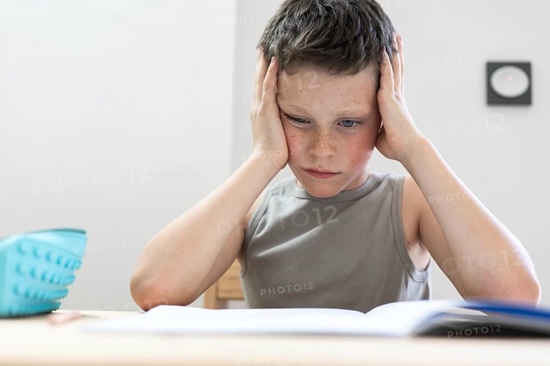 A young student intently reading a book, resting his head on his hands, illustrating focus and concentration, possibly facing challenges with homework or study