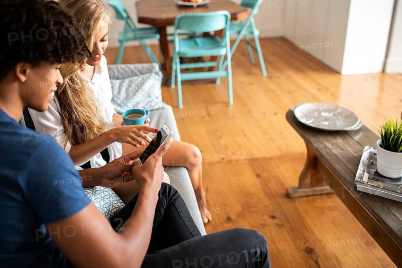 Cozy living room scene with a man and woman enjoying coffee and engaging with a smartphone. They share a peaceful moment, surrounded by modern and stylish decor