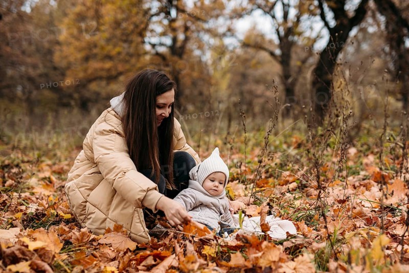 A mother and her child enjoy a beautiful autumn day in a park, sitting among colorful fallen leaves. The scene captures the warmth and joy of family moments in nature