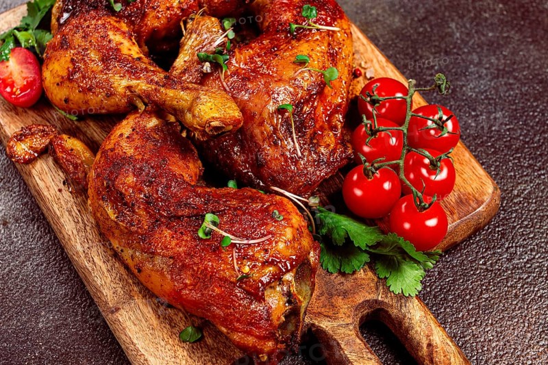 Grilled fried chicken legs, served with fresh cherry tomatoes, and herbs, on a wooden chopping board, homemade, no people