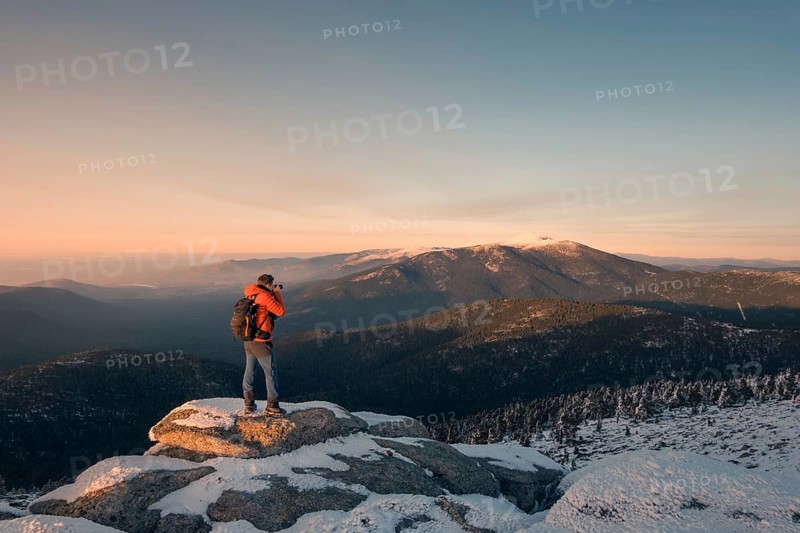 A photographer captures the serene, snowy landscape of Siete Picos in the Guadarrama Mountains, Madrid. The sunset bathes the peaks in a warm glow, highlighting the wintery scene