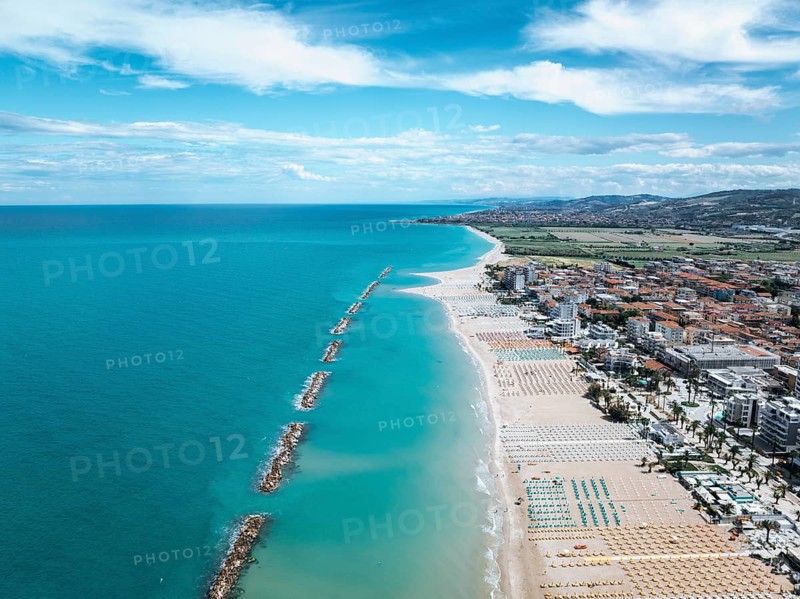 Stunning aerial photo of San Beneddetto, Italy, showcasing a vibrant blue sea meeting sandy beaches. Rows of colorful umbrellas line the shore