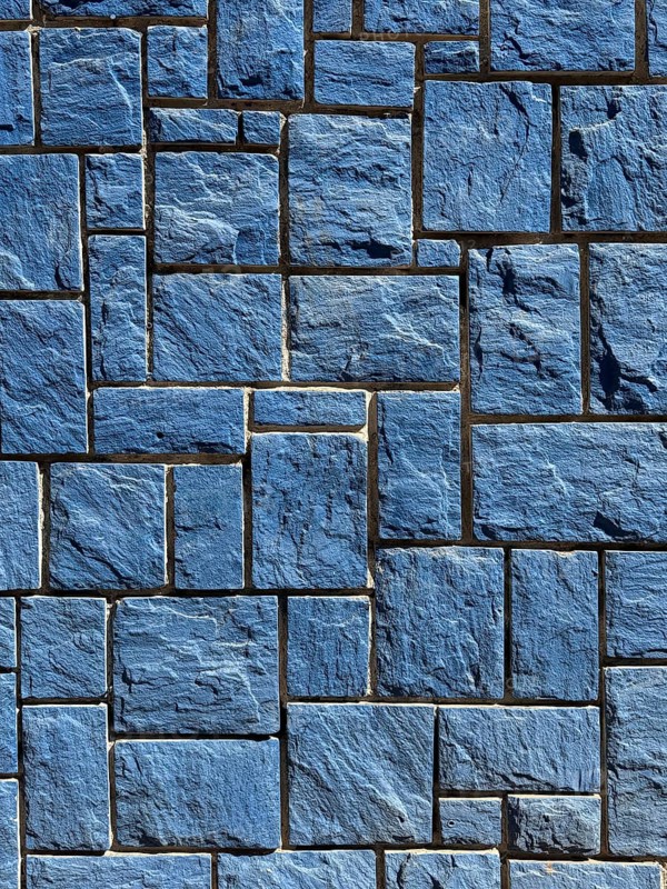 A detailed image of a blue stone wall featuring interlocking rectangular tiles with a rough texture. The stones are arranged in a geometric pattern providing a modern architectural look