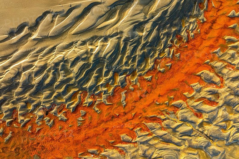 A mesmerizing aerial view of sand dunes with striking orange and beige hues, showcasing the beauty of nature patterns and textures in a captivating landscape