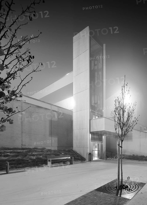 Black and white image of a modern urban elevator structure on a foggy night, illuminated by ambient street lighting