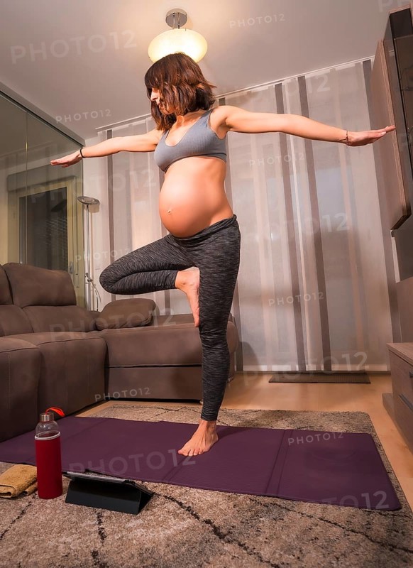 A young pregnant Caucasian woman doing pilates exercise at home in the living room. Online exercises in prepartum classes