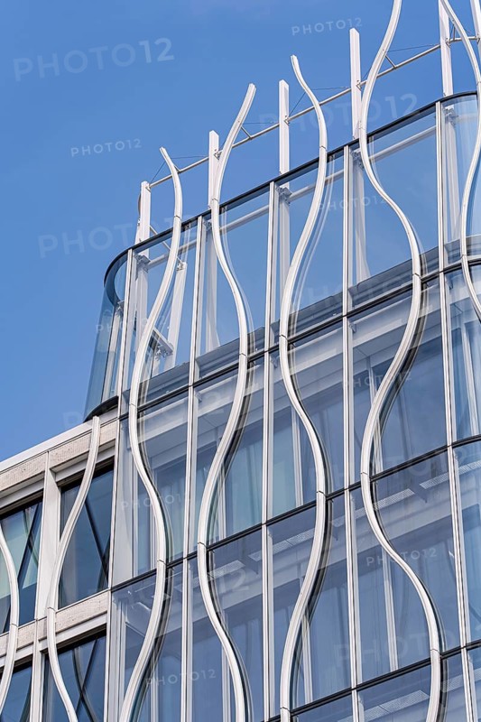 A modern building facade showcasing flowing metal and glass elements against a clear blue sky. The sleek curves and transparent surfaces highlight contemporary architecture