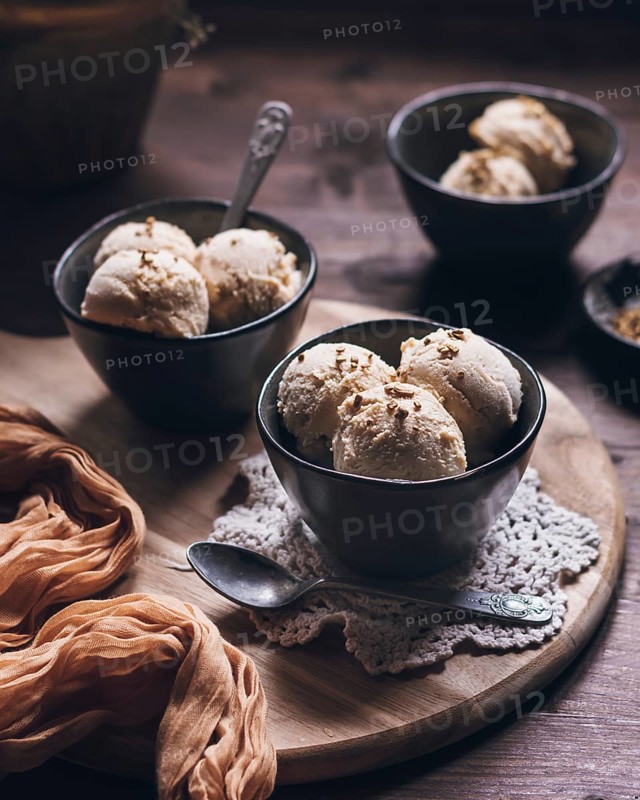 Three bowls of creamy peanut butter ice cream made with Greek yogurt and cream, presented in a rustic setting. A deliciously rich and flavorful dessert treat