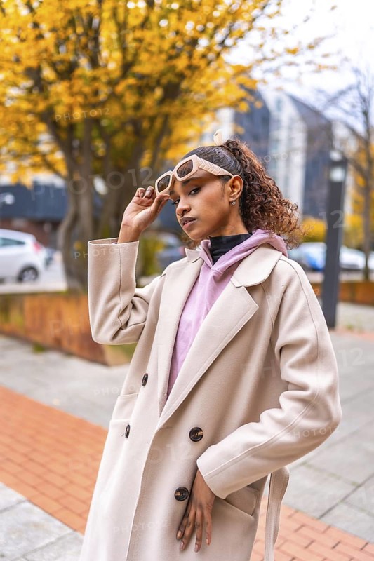 Vertical portrait of an african american model holding sunglasses wearing coat at city