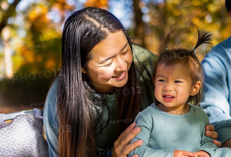 Asian family enjoying a sunny autumn day at the park, sharing joyful moments together. A mother and child are seen smiling, surrounded by colorful fall foliage