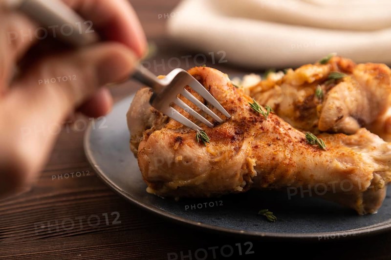 Fried Turkey Wing with spices and thyme on plate with hand on brown wooden background and linen textile. side view, close up, selective focus