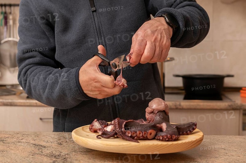 A man skillfully prepares fresh octopus on a wooden plate in a kitchen setting. This image captures the intricate detail of the culinary process and craftsmanship
