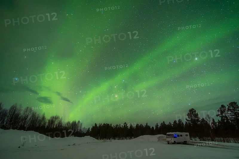 Stunning display of the Aurora Borealis near Kiruna, Sweden. The sky glows with breathtaking, ethereal green hues while the remote landscape and a solitary caravan enhance the scene's serene, mystical feel