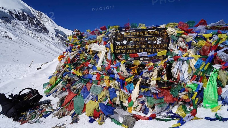 Colourful prayer flags and signs at Thorong La Pass under clear skies, trekking at Annapurna Circuit, Nepal