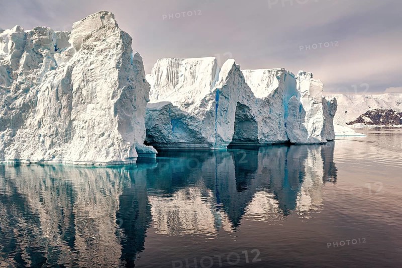 Massive iceberg with clear reflection in the water, against a blue sky, icebergs in the landscape of the Southern Ocean in Antarctica