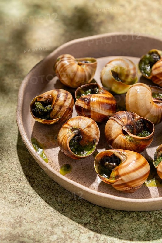Baked escargots garnished with fresh parsley and drizzled with melted butter, served in a rustic ceramic dish, under natural light