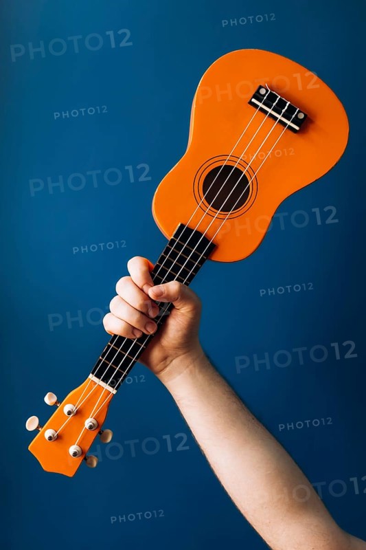 A person holds a bright orange ukulele, standing out against a clean blue background. This vibrant image captures the essence of musical expression and creativity