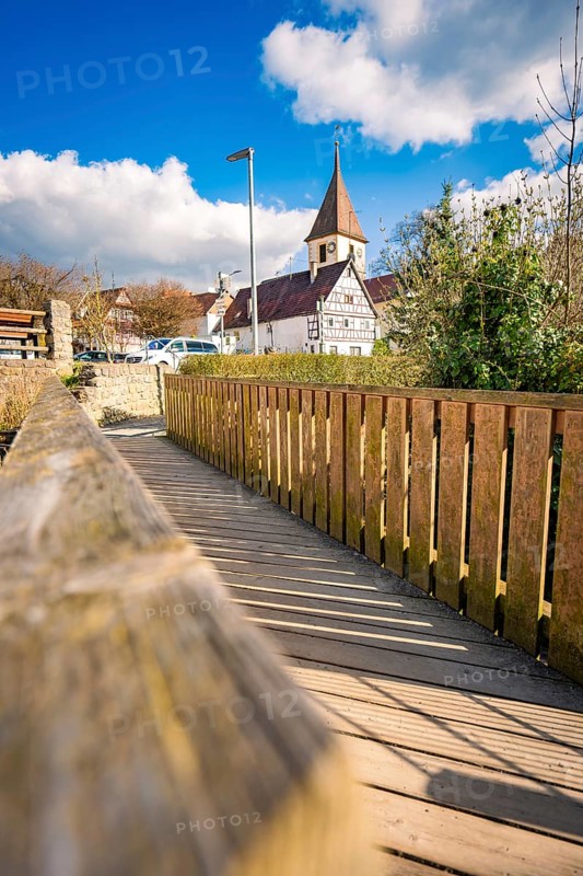 The wooden walkway and fence lead to the village church on a sunny day with clear skies, Deufringen, Aidlingen, Böblingen district, Germany