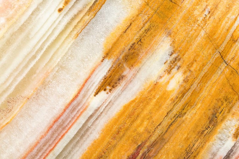 Detailed macro image of layered chalcedony, showcasing its parallel banding in warm golden, cream, and orange hues A stunning form of cryptocrystalline quartz with intricate textures