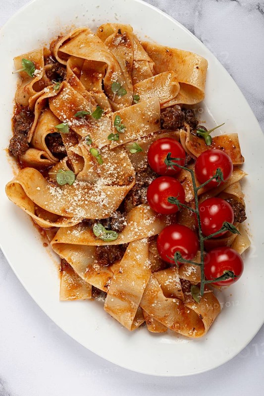 Pappardelle pasta with bolognese sauce, topped with parmesan cheese and cherry branch, homemade, no people