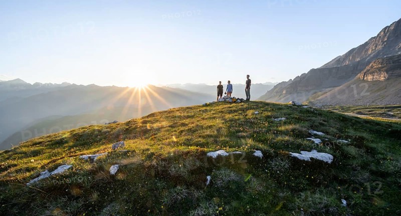 Three friends enjoy the sunset over the Adamello Group, mountainous landscape on the Grosté Plateau, Brenta Mountains, Trentino, Italy
