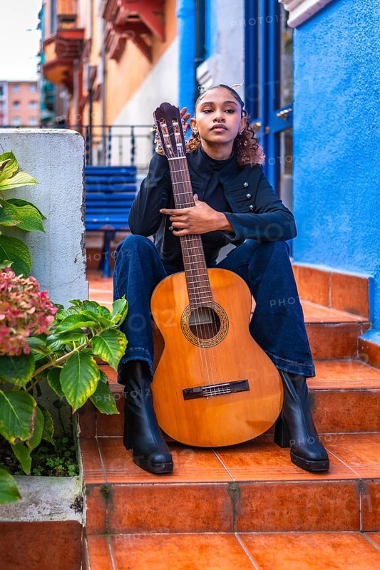 Portrait of a female african american musician with acoustic guitar sitting in outdoor stairs