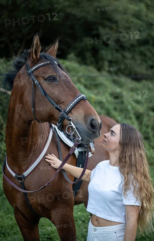 A young woman lovingly interacts with her horse, showcasing a special bond. The pair stands in a lush, green outdoor setting, emphasizing connection and nature's serenity