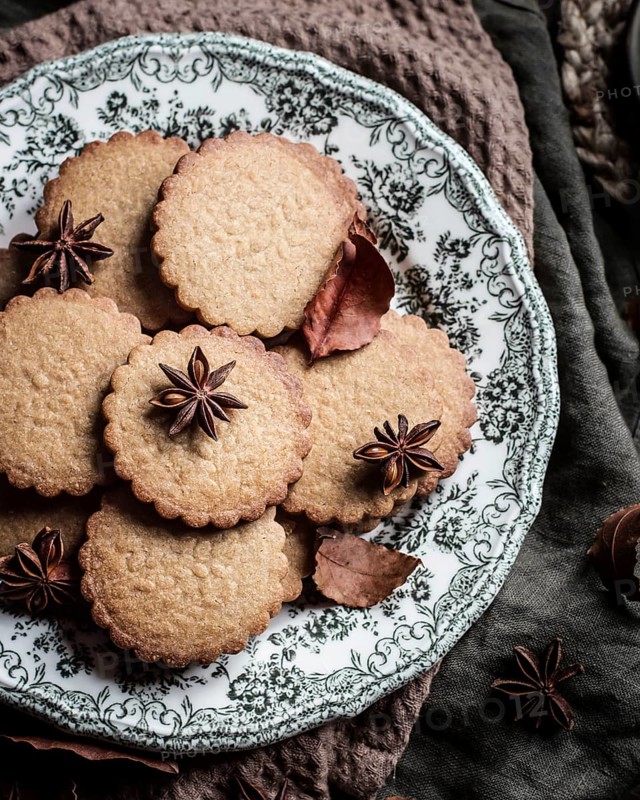 An artistic presentation of spiced cookies garnished with star anise, served on an intricately designed vintage plate, capturing a warm and inviting atmosphere