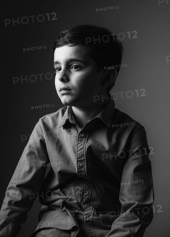 A black and white portrait of a young boy looking thoughtfully into the distance. The soft lighting and shadows create a calm and reflective mood, emphasizing his serene expression