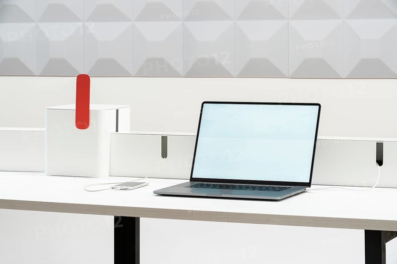 A sleek, minimalist workspace in office features a laptop and smartphone on a white desk, ideal for productivity. The setup is modern, with clean lines and minimal clutter