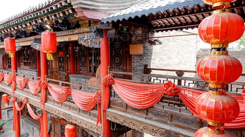 A traditional Chinese building in Pingyao, China, adorned with vibrant red lanterns and drapes. The intricate wooden carvings highlight the architectural beauty of the historical site